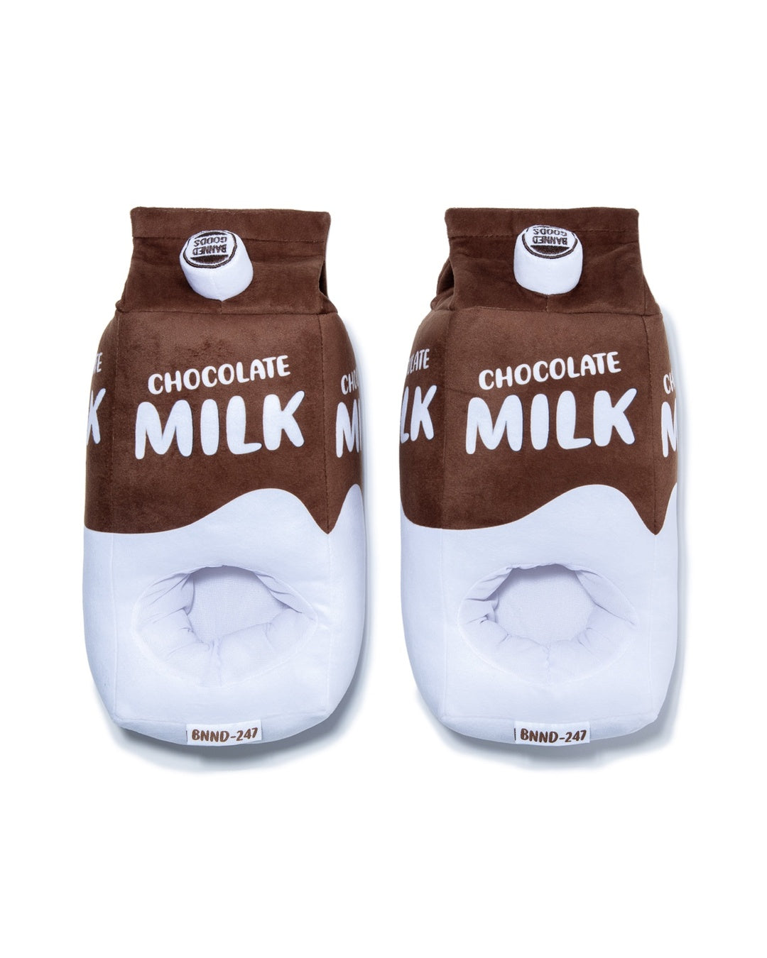 A pair of plush slippers designed to look like chocolate milk cartons, featuring a brown top half with white 'CHOCOLATE MILK' text, a white middle section, and a brown bottom edge, shown on a plain white background.
