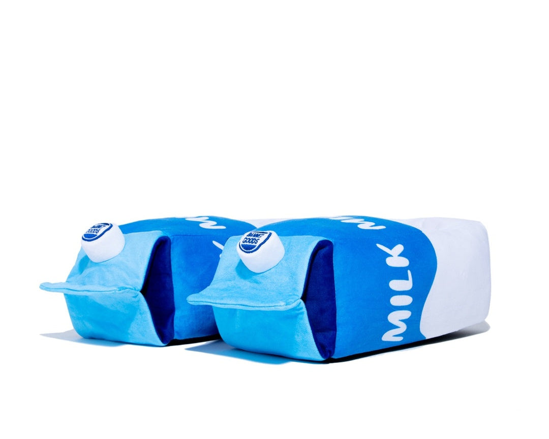Two plush slippers designed to look like milk cartons, featuring blue and white colors with the word 'MILK' printed on them, set against a plain white background.